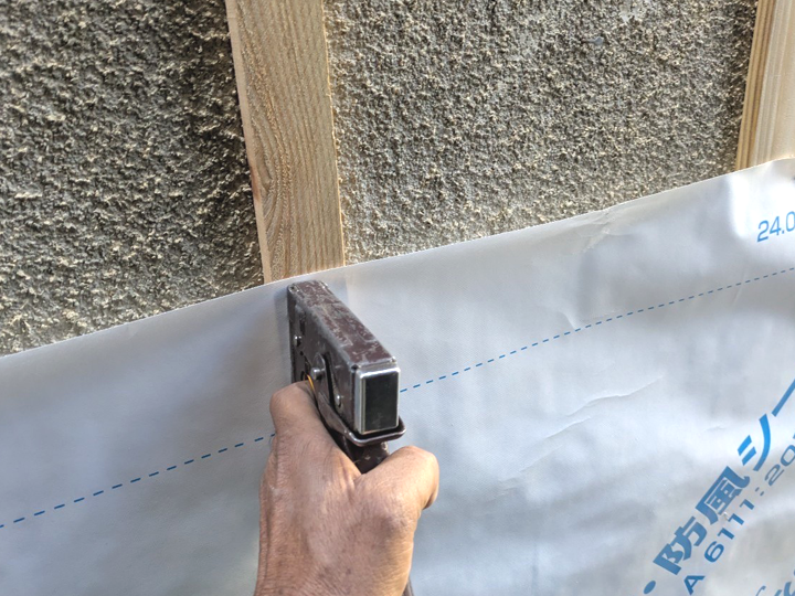 下地となるモルタル外壁に防水紙を施工している様子